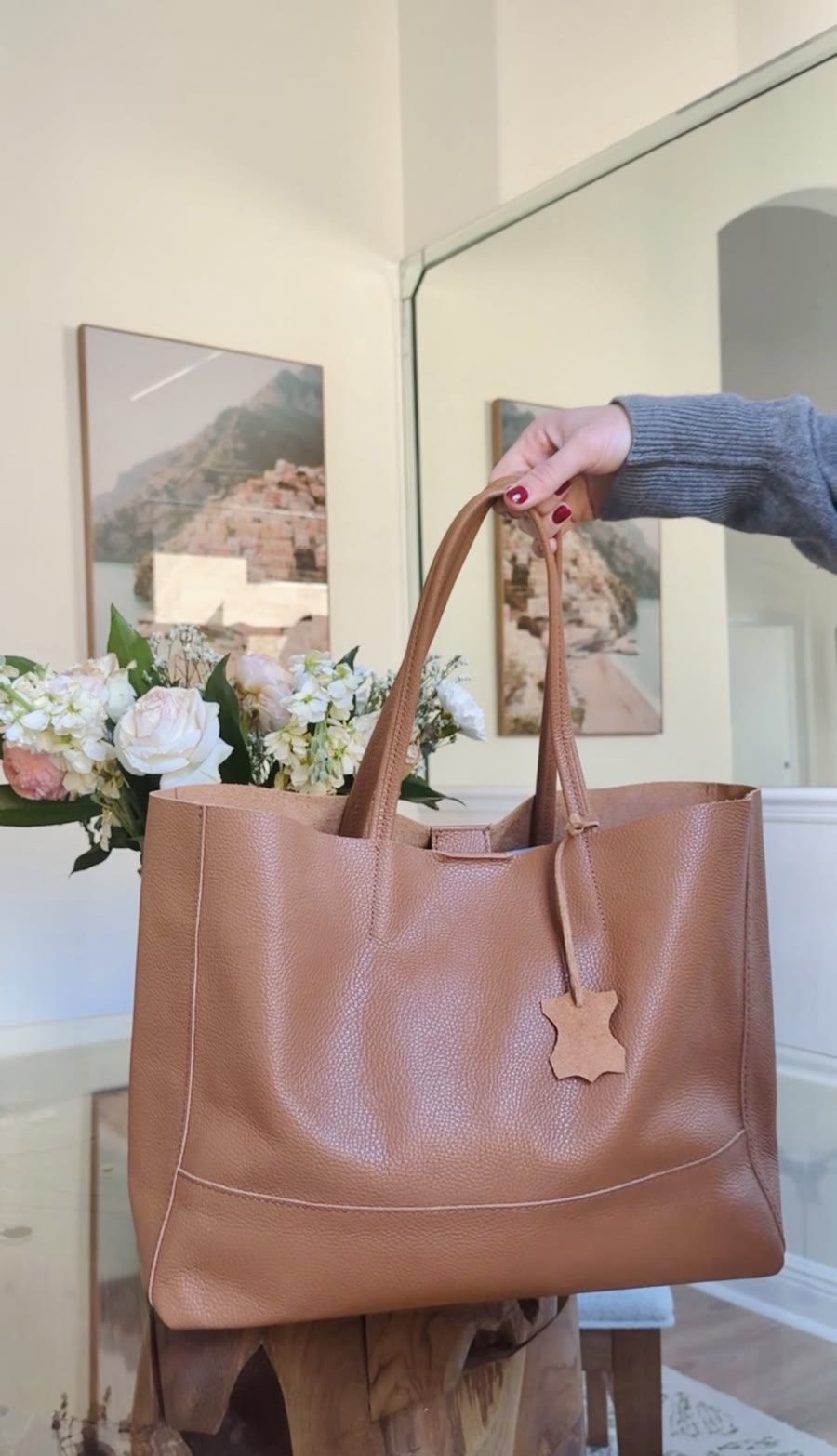 Hand holding a tan leather tote bag