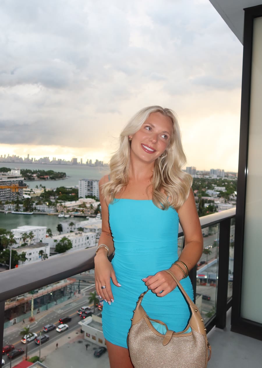 Molly in a teal dress on a balcony with the city skyline behind her